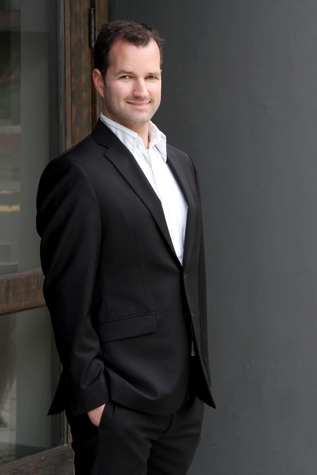 Joseph Olson in a dark suit, standing by a window