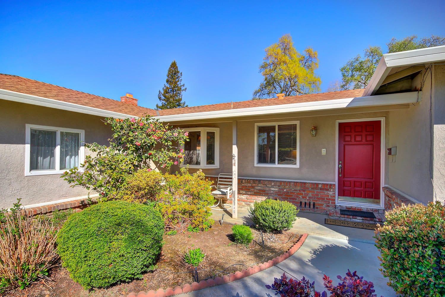 A single-story home with a red front door and a garden walk